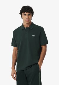 Donkergroen poloshirt gemaakt van katoen, met een klassieke kraag, een twee-knopen sluiting en een klein Lacoste-logo op de borst.