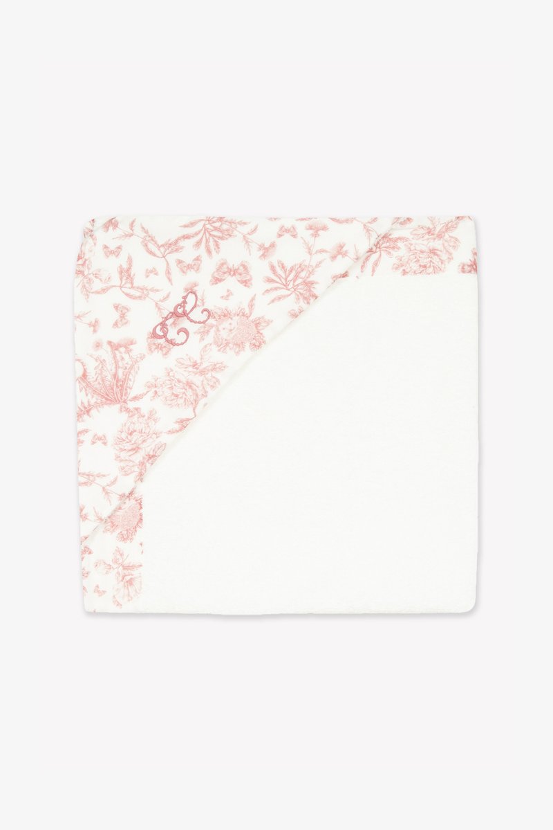 Λευκή κουβέρτα με ροζ λουλουδάτο σχέδιο που περιλαμβάνει πεταλούδες και φυτά. Σε μια γωνία φαίνεται υφασμάτινη υφή με κεντημένες λεπτομέρειες.