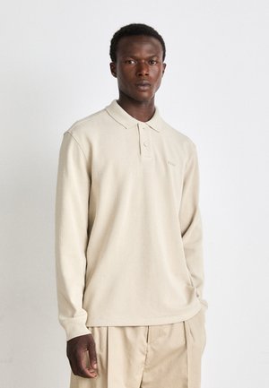 Polo a maniche lunghe beige in tessuto strutturato con colletto morbido, chiusura a tre bottoni e logo discreto sul petto.
