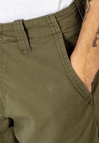 Olivgrüne Cargo-Shorts aus Baumwolle mit einem Gürtelschlaufen, Fronttasche und einer glatten Textur; sichtbare Nähte akzentuieren die Kanten.
