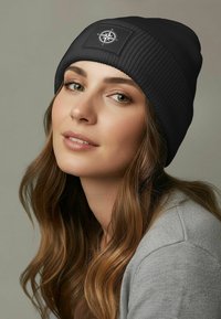 Black ribbed knit beanie featuring a front patch with a compass design. The beanie has a flexible shape and a textured surface for warmth.