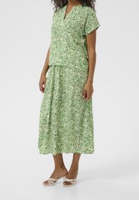 Groene bloemen maxi-jurk met korte mouwen, v-hals en vloeiende rok. Gemaakt van lichtgewicht stof met een zachte textuur. Ggedragen met witte sandalen.
