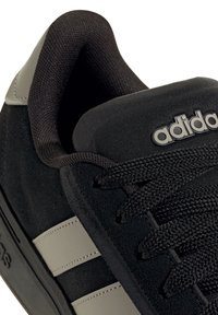 Nahaufnahme eines schwarzen Adidas Sneakers mit strukturierten Stoffsenkeln, gepolstertem Kragen und grauen synthetischen Streifen an der Seite.