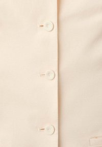 Gros plan sur un tissu beige avec trois boutons ronds cousus verticalement le long d'une couture.