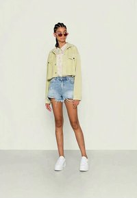 Izgriezta gaiši zaļa jaka, ziedu krekls, nolietoti džinsu šorti un balti sporta apavi. Izskatu papildina apaļas rozā saulesbrilles.