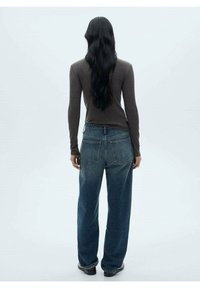 Un haut marron ajusté à manches longues associé à un jean en denim bleu délavé, ample, avec un design classique à cinq poches et des coutures visibles.