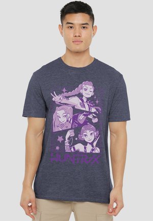 Man wearing navy blue T-shirt with purple anime-style characters and "HUNTR/X" text on front.