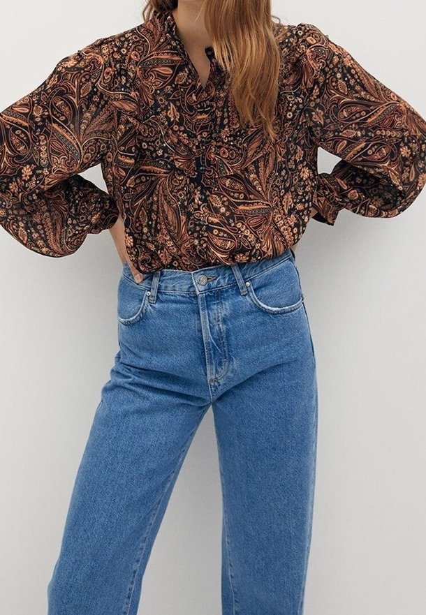 Blouse à manches longues en tissu foncé avec un motif cachemire orange et marron ; associée à un jean taille haute droit bleu clair.