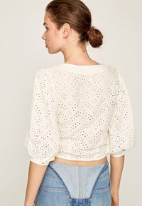 Top bianco a maniche corte con un motivo goffrato ad orecchiette, maniche a sbuffo e scollatura rotonda, abbinato a un pantalone di denim.