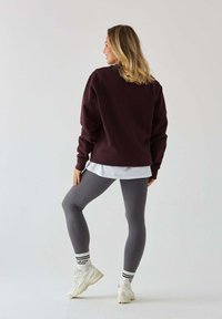 Burgundowa, oversize'owa bluza połączona z szarymi, ribbed legginsami i białymi sneakerami. Charakteryzuje się warstwowym wyglądem, z białą koszulą pod spodem.