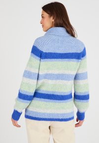 Maglione a righe blu e verde con colletto alto, texture a costine e maniche lunghe. Il motivo alterna righe spesse e sottili.