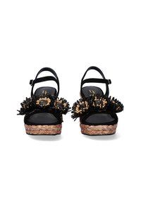 Zapatos de charol negros tipo slingback con adornos florales, suela de plataforma de yute trenzado y correas para el tobillo. Textura de cuero suave.