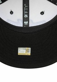 Gorra negra con visera plana, el interior presenta un forro blanco, etiqueta con código QR y texto, y pequeños agujeros de ventilación a lo largo de la corona interior.
