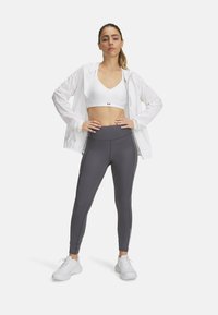 Veste zippée blanche sur un soutien-gorge de sport blanc, associée à des leggings gris avec des coutures latérales et des accents blancs, le tout complété par des baskets blanches.