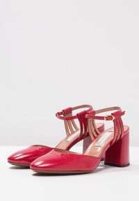 Chaussures à talons hauts en cuir rouge avec un bout pointu, une bride à la cheville et un talon épais. Présentent une texture lisse et un éclat subtil.