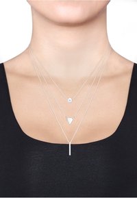 Silberne geschichtete Halsketten mit einem kleinen runden Anhänger, einem dreieckigen Charm und einem vertikalen Balkenanhänger an feinen Ketten. Elegantes und minimalistisches Design.