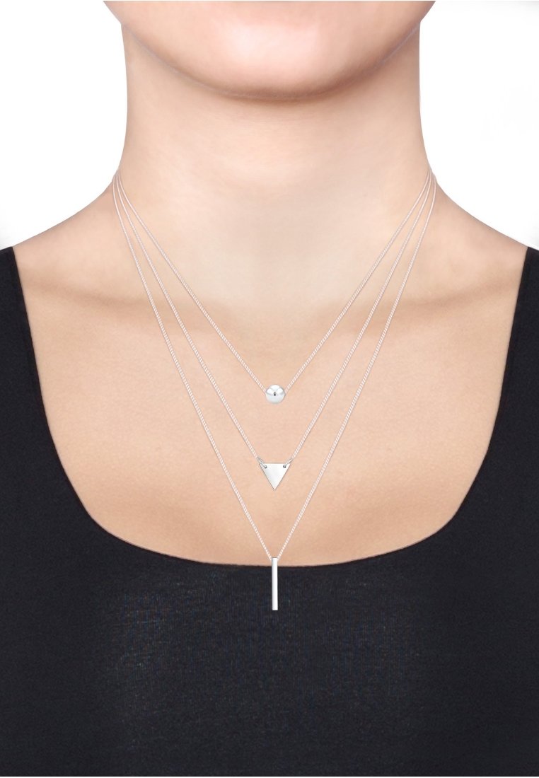 Silberne geschichtete Halsketten mit einem kleinen runden Anhänger, einem dreieckigen Charm und einem vertikalen Balkenanhänger an feinen Ketten. Elegantes und minimalistisches Design.