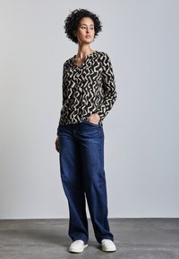 Top a maniche lunghe nero e crema con motivo, abbinato a jeans a gamba larga blu scuro e sneakers bianche, caratterizzato da una vestibilità comoda.