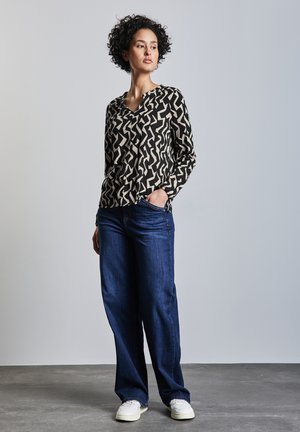 Black and cream patterned long-sleeve top paired with dark blue wide-leg jeans and white sneakers, featuring a relaxed fit.