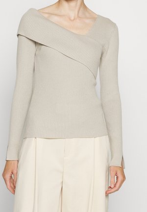 Beigenvärinen, ribbineulottu olkapäiden paljastava neulepaita, jossa on pitkät hihat, yhdistetty vaalean kermanvärisiin korkeavyötäröisiin leveälahkeisiin housuihin.