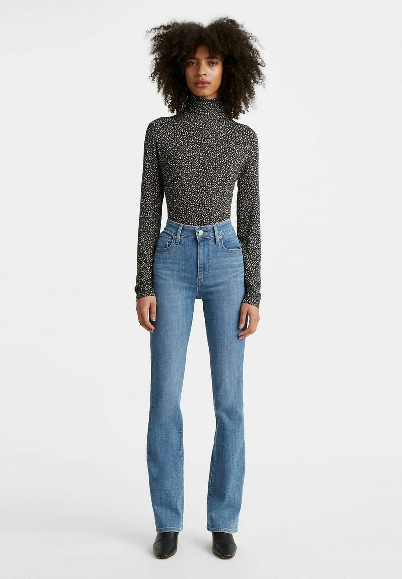 Zwarte lange mouwen top met een bloemendessin, gecombineerd met lichtblauwe high-waisted flared jeans en zwarte enkellaarzen.