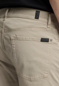 Ljust beige byxor i bomull med en bakficka som har en tygetikett och synliga sömdetaljer.