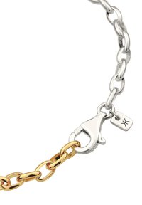 Kettenarmband mit abwechselnden Gold- und Silbergliedern, ausgestattet mit einem Karabinerverschluss und einem kleinen Anhängerschild. Glatte, polierte Metalloberflächen.