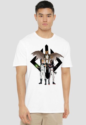Young man wearing white t-shirt with graphic of three superheroes, one with wings holding a staff, standing against a black geometric background.