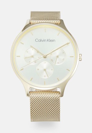 Goldfarbene Uhr mit Mesh-Armband, einem hellgrünen Ziffernblatt, drei Teilzifferblättern, minimalistischen Stundenziffern und dem Calvin Klein-Logo oben.