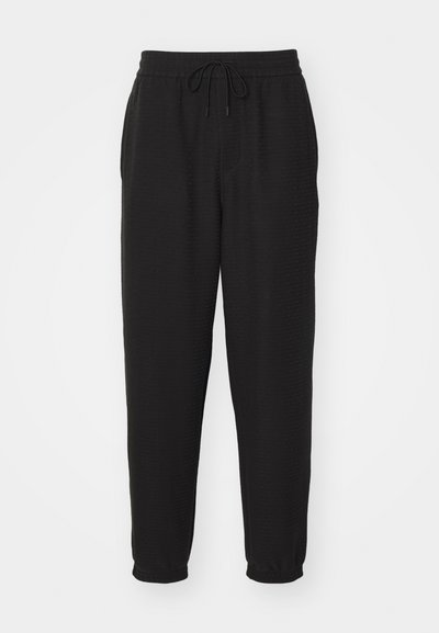 Černé joggingové kalhoty vyrobené z texturované tkaniny, s elastickým pasem a stahovací šňůrkou, a zúženými nohavicemi.