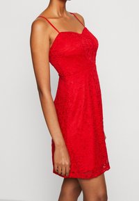 Abito rosso in pizzo con spalline sottili, corpetto aderente e gonna svasata. Motivo floreale su tutta la superficie, tessuto strutturato, lunghezza a metà coscia.