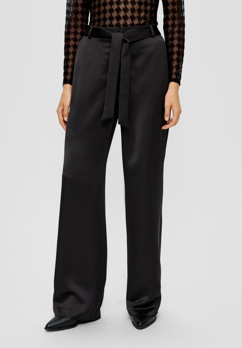 Pantalon noir à jambes larges en tissu lisse, avec ceinture nouée à la taille. Design innovant avec une silhouette ajustée et une brillance subtile.