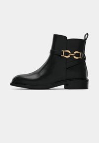 Botas de tornozelo em couro preto com biqueira arredondada, salto baixo e detalhes em metal dourado. Apresenta uma tira decorativa e um laço na parte de trás.