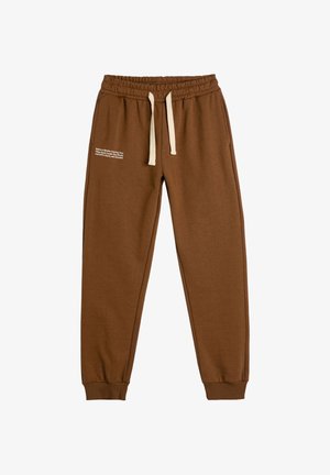 Musta jogger-housut elastisella vyötäröllä ja kermanvärisillä nauhoilla, taitetut nilkat ja valkoinen teksti vasemmassa reidessä.