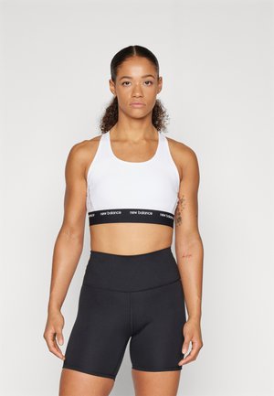 Hvit sports-bh med svart elastisk bånd med "new balance" logo, sammen med høyt midje svarte shorts, glatt tekstur, tettsittende design.