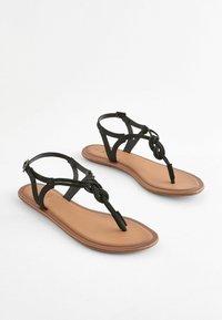 Zwarte leren slipper sandalen met een geknoopte design, platte tan zool en verstelbare enkelbandjes. Gladde textuur, minimalistisch ontwerp.