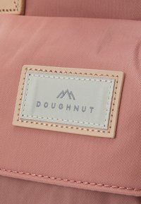 Doughnut brand tag on a pink fabric surface, featuring a textured finish with a cream label, black lettering, and a mountain graphic.