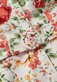 Bloemstof met grote rode en gele bloemen op een witte achtergrond. Inclusief een met stof bedekte ronde gesp als ontwerpelement.