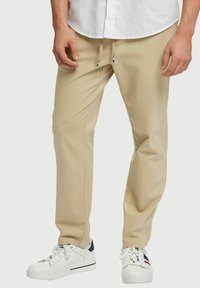 Beige rechte broek met verstelbare trekkoord in de taille, voorzien van zijzakken en subtiele stiksels, gecombineerd met witte sneakers.