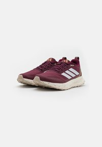 Chaussures de sport bourgogne avec une tige texturée, arborant trois bandes blanches, une semelle beige avec des éclaboussures, et un talon renforcé pour un soutien optimal.