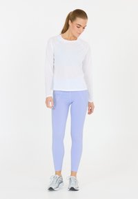 Långärmad vit atletisk topp i kombination med ljuslila leggings. Kläderna har en kroppsnära design med platta sömmar och luftigt tyg.