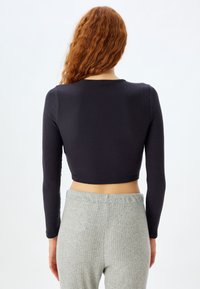 Sort ribbet langærmet crop top med rund halsudskæring, parret med lysegrå ribbet højtlivet bukser. Teksturerede materialer synlige.