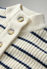 Cremefarbener, gestrickter Pullover mit marineblauen horizontalen Streifen, geripptem Kragen und drei hellbraunen Knöpfen auf der vorderen Blende.