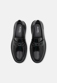 Paire de mocassins en cuir noir brillant avec bouts arrondis et design sans lacets, marque ALDO sur la semelle intérieure, présentée vue de dessus sur fond blanc.