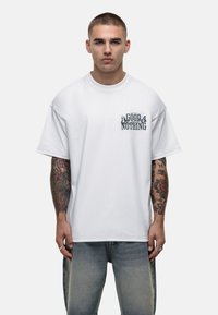 Biała, oversize koszulka z krótkimi rękawami i okrągłym dekoltem, z graficznym nadrukiem "GOOD FOR NOTHING" na piersi, wykonana z bawełny.