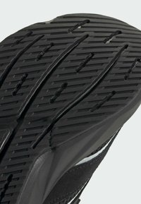 Čierna gumová podrážka topánky s hlbokým vzorom dezénu, obsahujúca horizontálne drážky a vertikálne rezy pre lepšiu trakciu. Hladké okraje a zaoblený opätok.