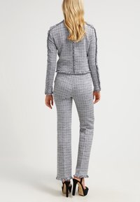 Grå och vit tweedkostym med fransade kanter, figursydd jacka och raka byxor. Klackskor förbättrar outfitens övergripande utseende.