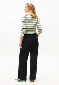 Sweter w paski w odcieniach zieleni, czerni i beżu, zestawiony z czarnymi spodniami. Charakterystyczne cechy to krótki krój i luźna sylwetka.