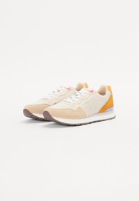Baskets de sport beiges en matériaux en daim et en maille, avec une semelle intermédiaire blanche, des lacets roses et des accents orange et violet sur le talon.