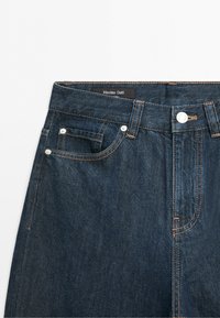 Dunkelblauer Jeansbund mit vorderer Knopfleiste, Gürtelschlaufen, Münztasche und sichtbarem Massimo Dutti-Label.